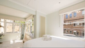 Ein Schlafzimmer mit einem großen Bett, einem Fenster mit Blick auf ein Backsteinhaus und einer Heizung.