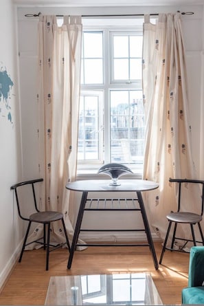 Een kamer met een ronde tafel, twee stoelen, een raam met gordijnen en een kaart aan de muur.