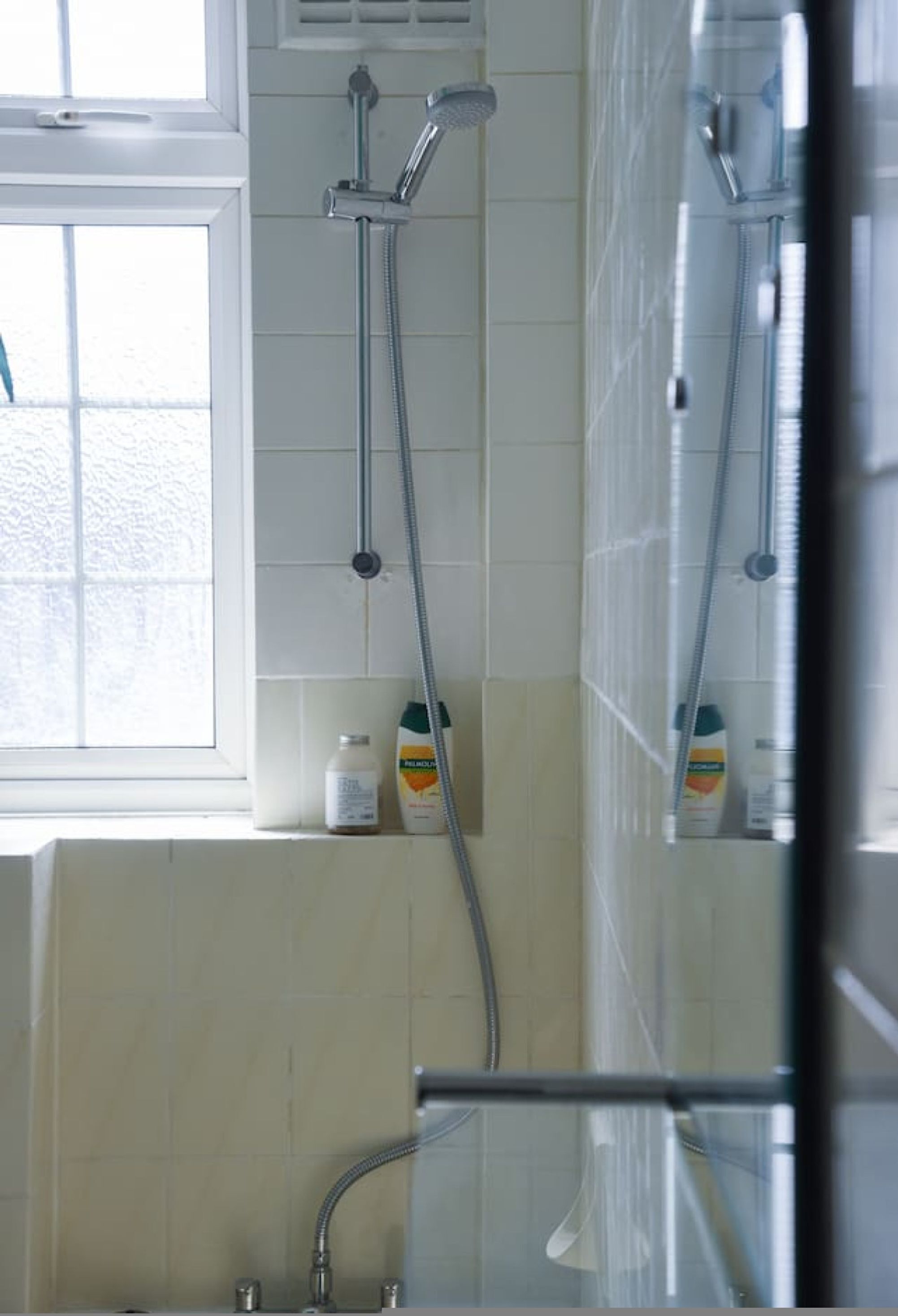 A bathroom with a shower, a window, and a bottle of shampoo on the wall.