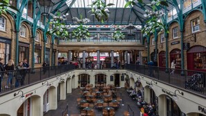 Een ruime overdekte markt met meerdere eetgedeeltes, een overdekt verdiep en diverse winkels.