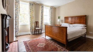 Een slaapkamer met een houten bed, een stoel, een open haard en een raam met gordijnen.