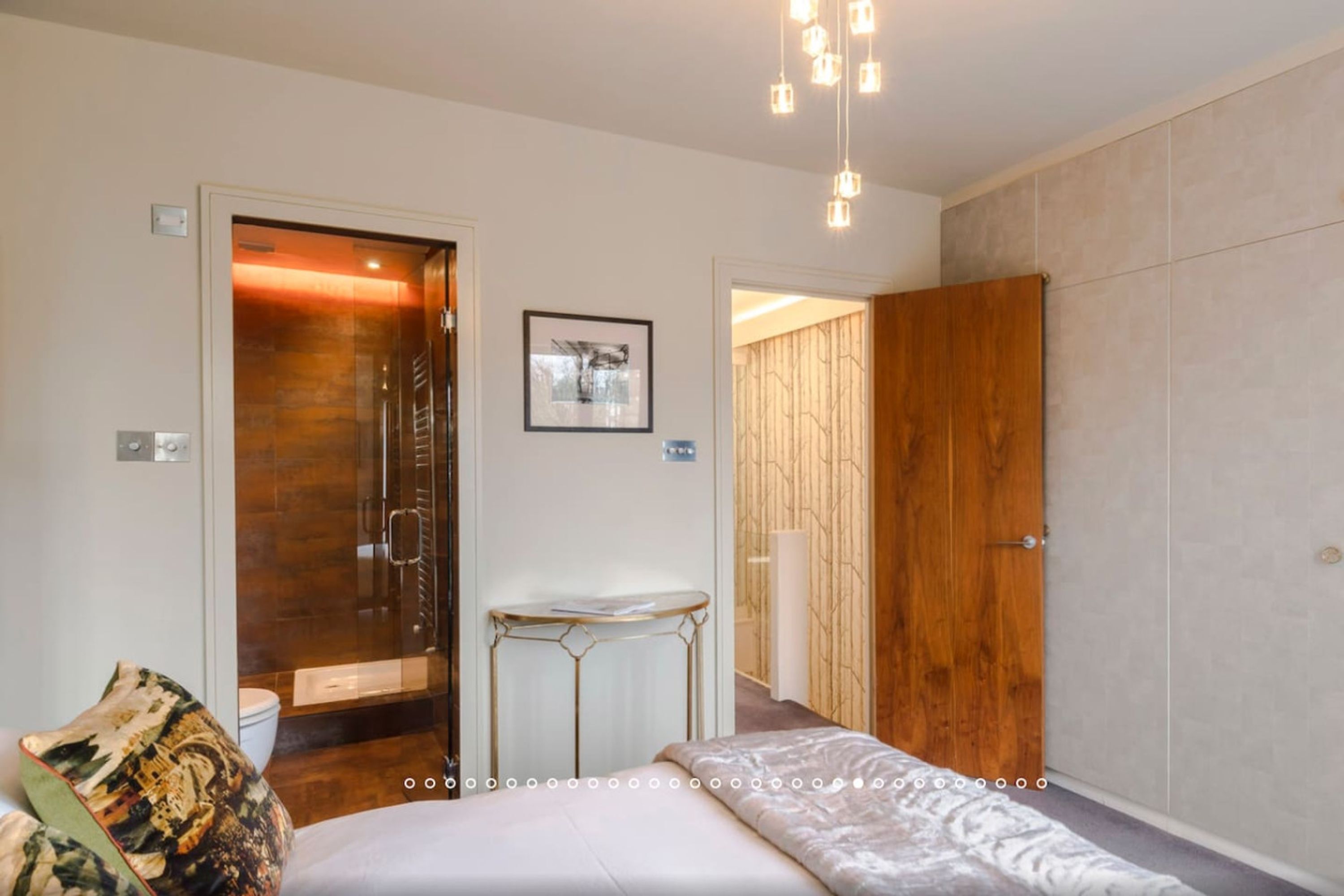 A modern hotel room with a bed, a small table, a shower area, and a wardrobe.