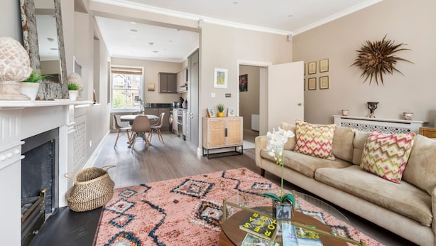 A living room with a sofa, coffee table, and a fireplace. There is a kitchen in the background. - Green Leafy 2 Bedroom in Clapham (London)