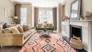 A living room with a sofa, a coffee table, a fireplace, and a large window. - Green Leafy 2 Bedroom in Clapham (London)