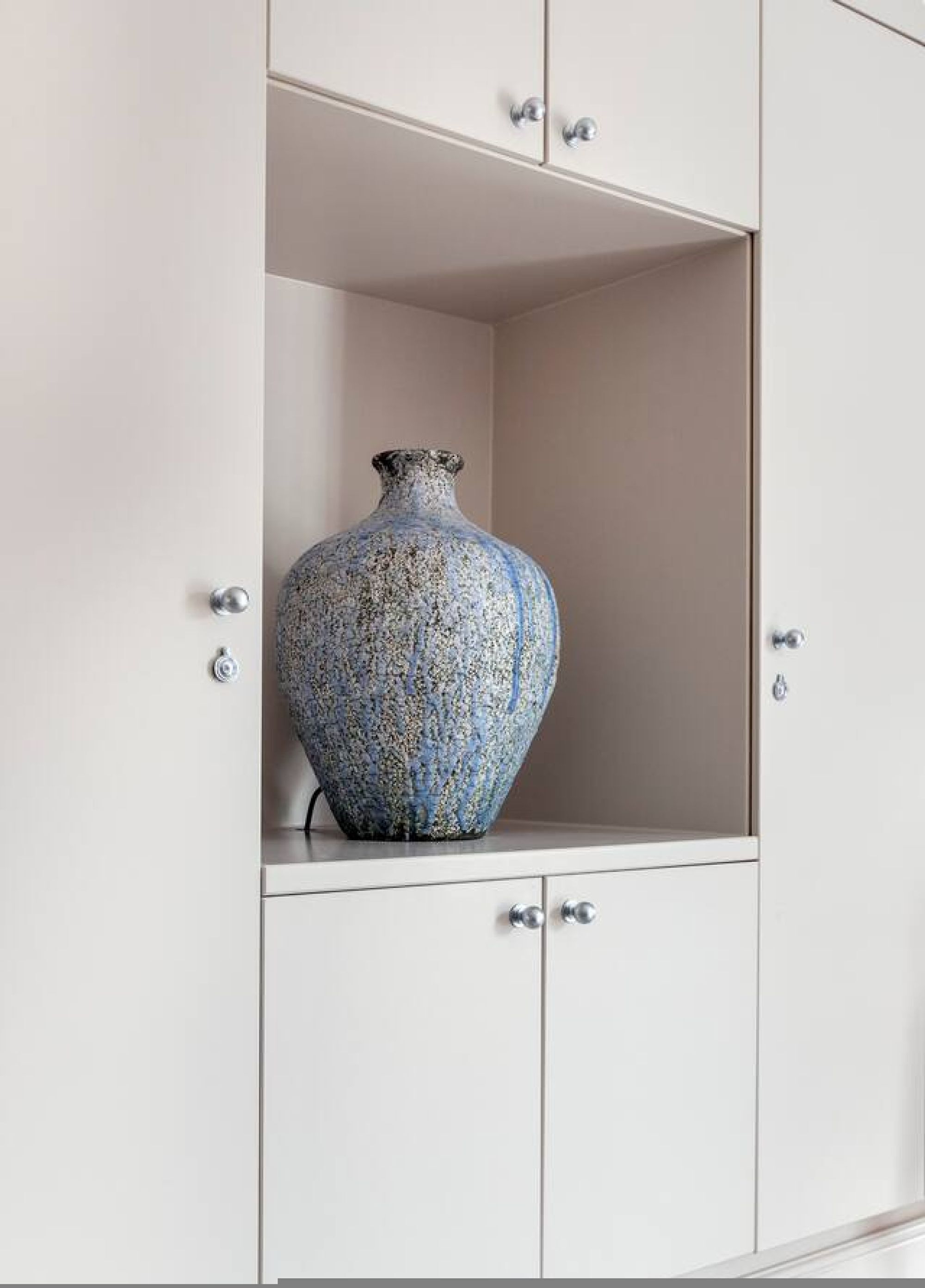 Un meuble blanc sur lequel est posé un vase bleu.