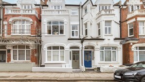 A row of Victorian-style townhouses with white and red brick facades, large windows, and a blue door. - Green Leafy 2 Bedroom in Clapham (London)