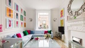 A modern living room with a sectional sofa, a glass coffee table, and a fireplace. - Cosy and Stylish Chelsea 2 Bedroom Flat (London)