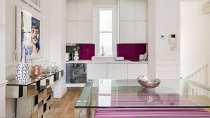 A modern kitchen with white cabinets, a glass table, and a pink accent wall. - Cosy and Stylish Chelsea 2 Bedroom Flat (London)
