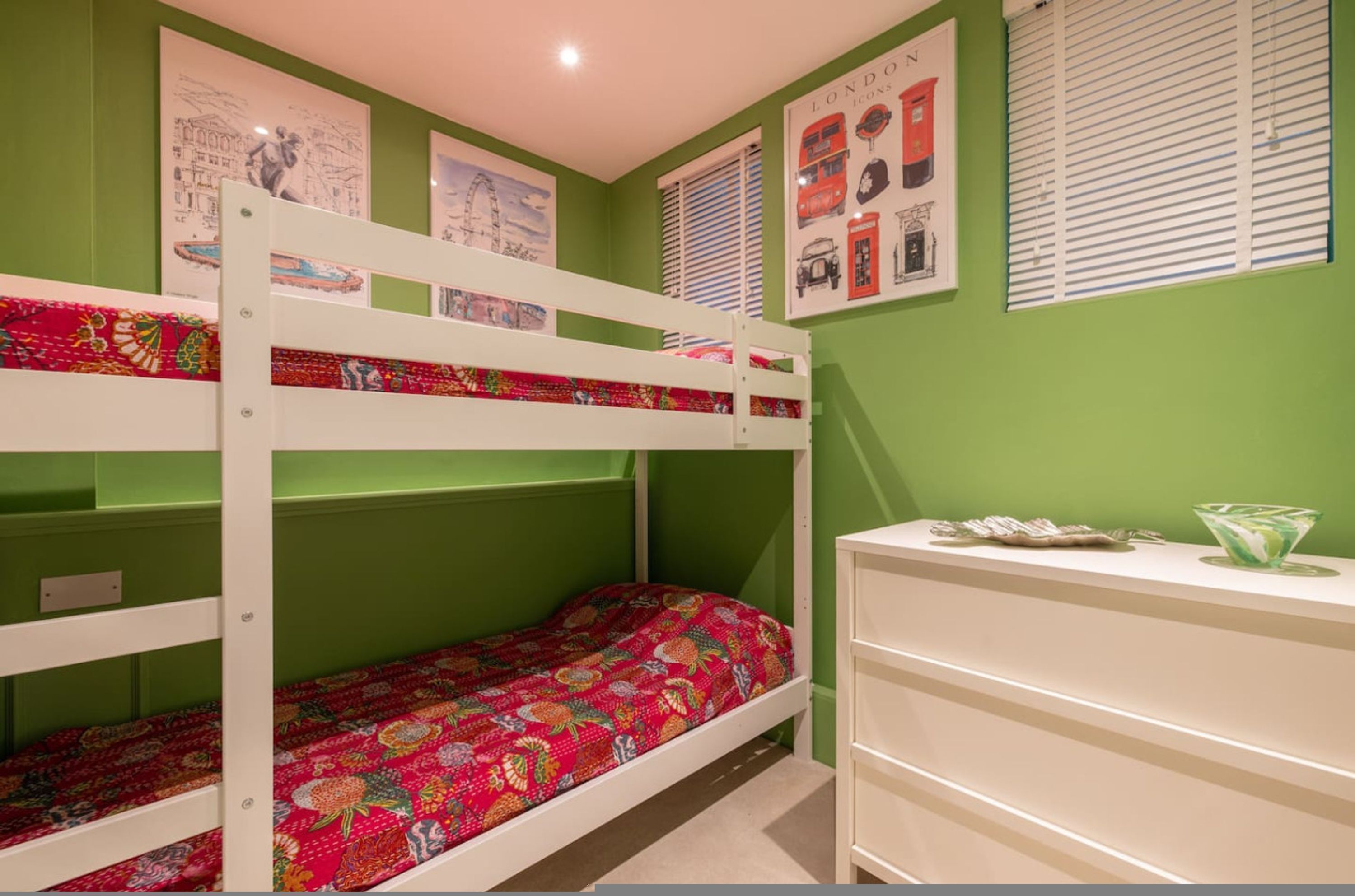 A bunk bed room with green walls, a white dresser, and a framed poster of London icons.