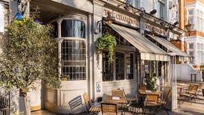 An outdoor seating area with tables and chairs, a hanging plant, and a building with a sign reading 'The Champion'. - Whoops-a-daisy 3 Bedroom in Notting Hill (London)