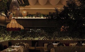 An indoor dining area with tables, chairs, hanging lamps, and a wall of greenery. - A Royal Residence Stylish 2 Bedroom in Kensington (London)