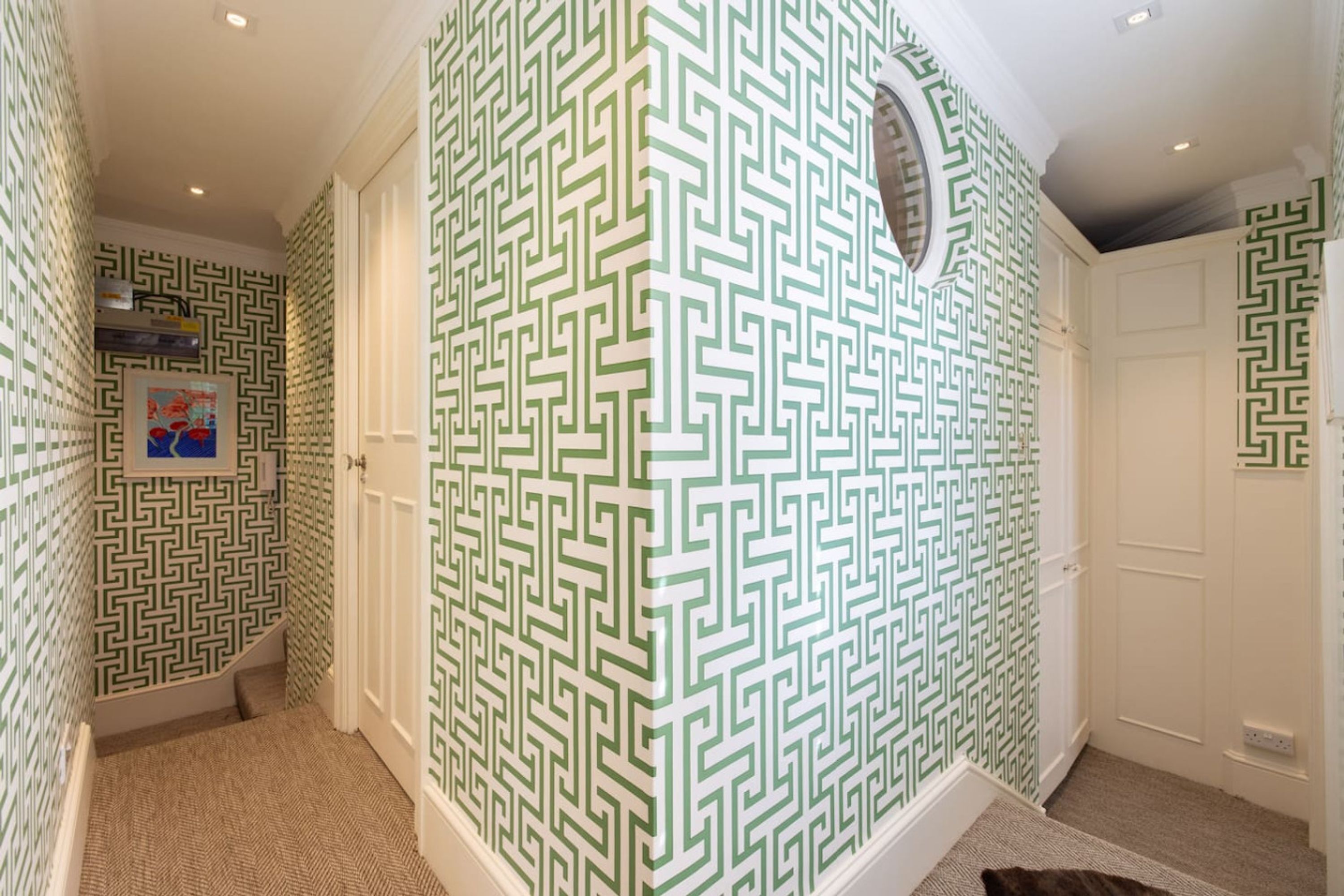 A hallway with patterned wallpaper, white doors, and a carpeted floor.