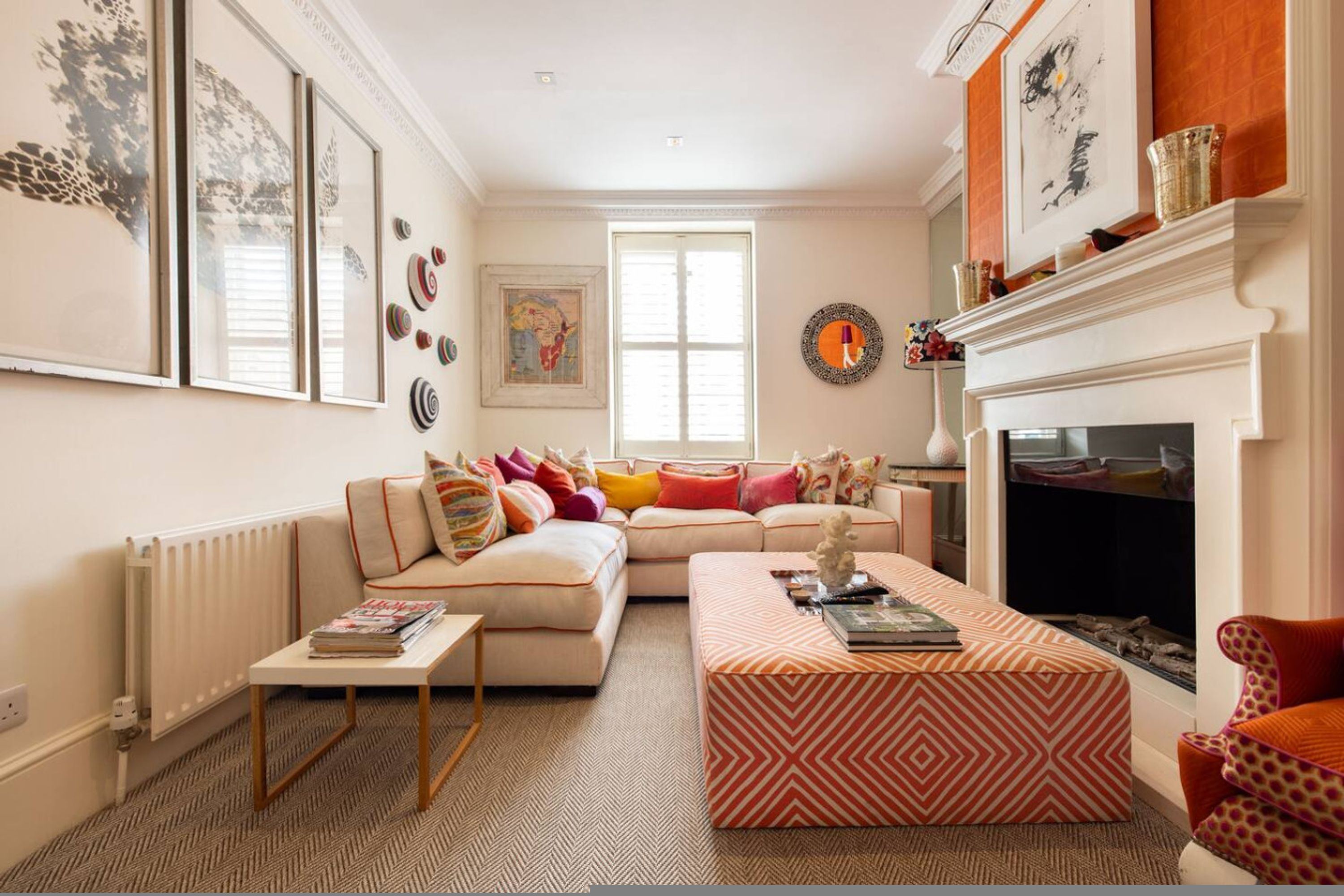A living room with a sofa, ottoman, fireplace, and artwork on the walls.