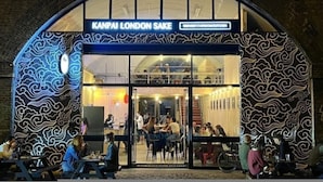 Een restaurant met een exterieur in golfpatroon en een bord waarop 'KANPAI LONDON SAKE' staat.