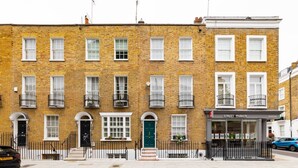 Un bâtiment en briques de deux étages, avec une porte verte, des fenêtres à cadre blanc et une clôture en métal noir.
