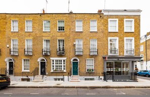 A two-story brick building with a green door, white-framed windows, and a black metal fence. - The Impressionist s Fireplace 4 BR Home in Chelsea (London)