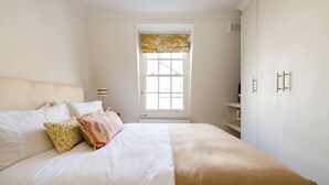 Un dormitorio con cama, almohadas, una ventana con cortinero y un armario.