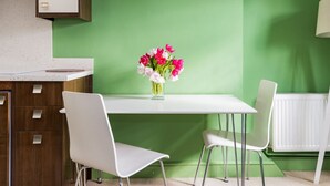 Un comedor con una mesa y sillas blancas, un jarrón de flores y una pared verde.