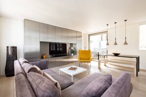 A modern living room with a sofa, a coffee table, a TV, and a yellow chair. - The Tonic 1 Bed With Patio in Shoreditch (London)