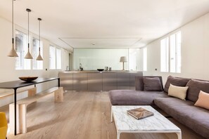 A modern living room with a sofa, a coffee table, and a dining area with a bench and table. - The Tonic 1 Bed With Patio in Shoreditch (London)