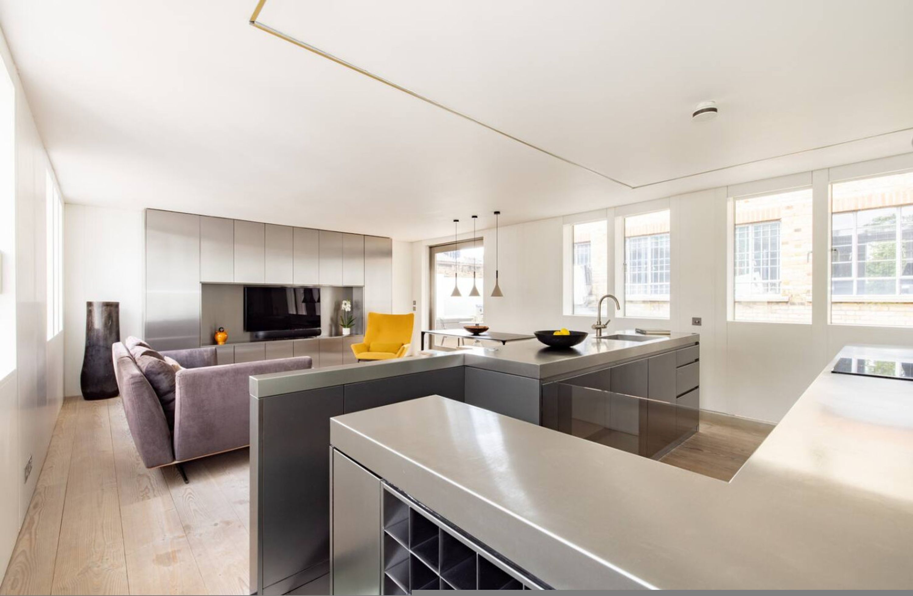 A modern kitchen with a central island, grey cabinetry, and a yellow chair.