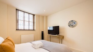 A hotel room with a bed, a television on a stand, a window with blinds, and a wall-mounted artwork. - London Muse 1 Bedroom Apartment in Belgravia (London)