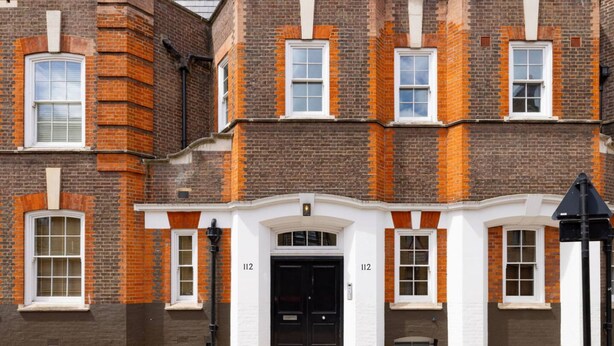 A multi-story brick building with a black front door, numbered 112, and white-framed windows. - London Muse 1 Bedroom Apartment in Belgravia (London)