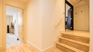 A hallway with wooden flooring, a staircase with a handrail, and a door with a sign above it. - London Muse 1 Bedroom Apartment in Belgravia (London)