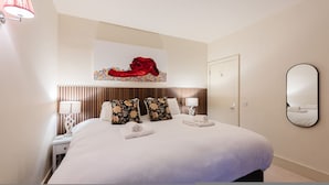 Une chambre d’hôtel avec un grand lit, une tête de lit à lattes verticales, deux lampes de chevet, un miroir fixé au mur et une œuvre d’art florale au-dessus du lit.