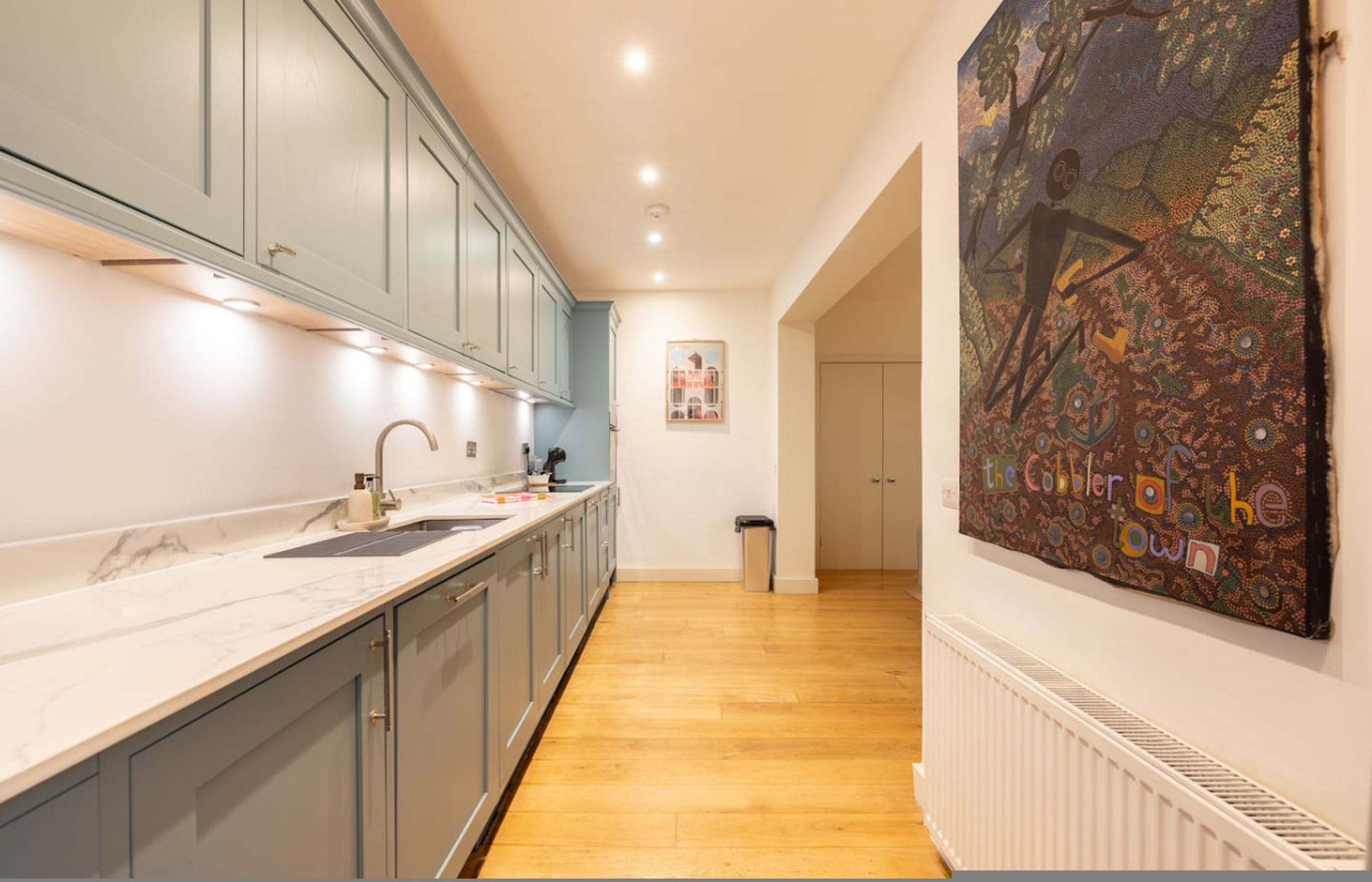 Eine moderne Küche mit grauen Schränken, einer Marmorarbeitsplatte und einem an der Wand hängenden Kunstwerk.