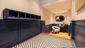 Un couloir avec un sol à carreaux, une chaise blanche, un miroir et une étagère sur laquelle sont posés divers objets.
