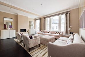Ein modernes Wohnzimmer mit einer Sofagarnitur, Sesseln, einem Couchtisch und einem Fernseher.