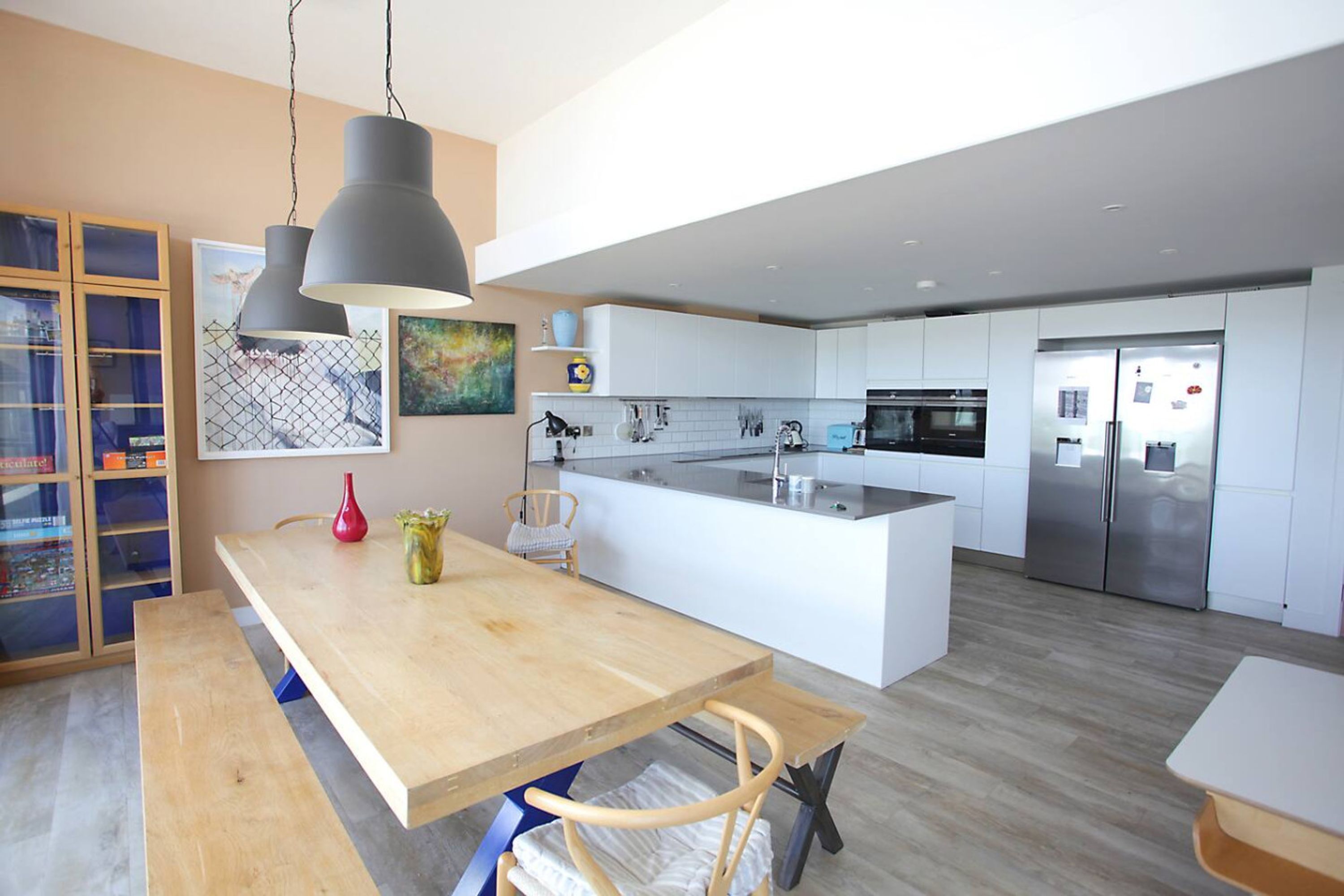 A modern kitchen with a central island, white cabinetry, stainless steel appliances, and pendant lighting.