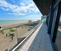 Un balcón con vista a la playa y al mar, piso de baldosas y barandilla.