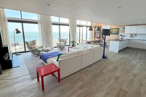 Un salón moderno con un sofá blanco grande, una mesa roja y vistas al mar a través de amplios ventanales.