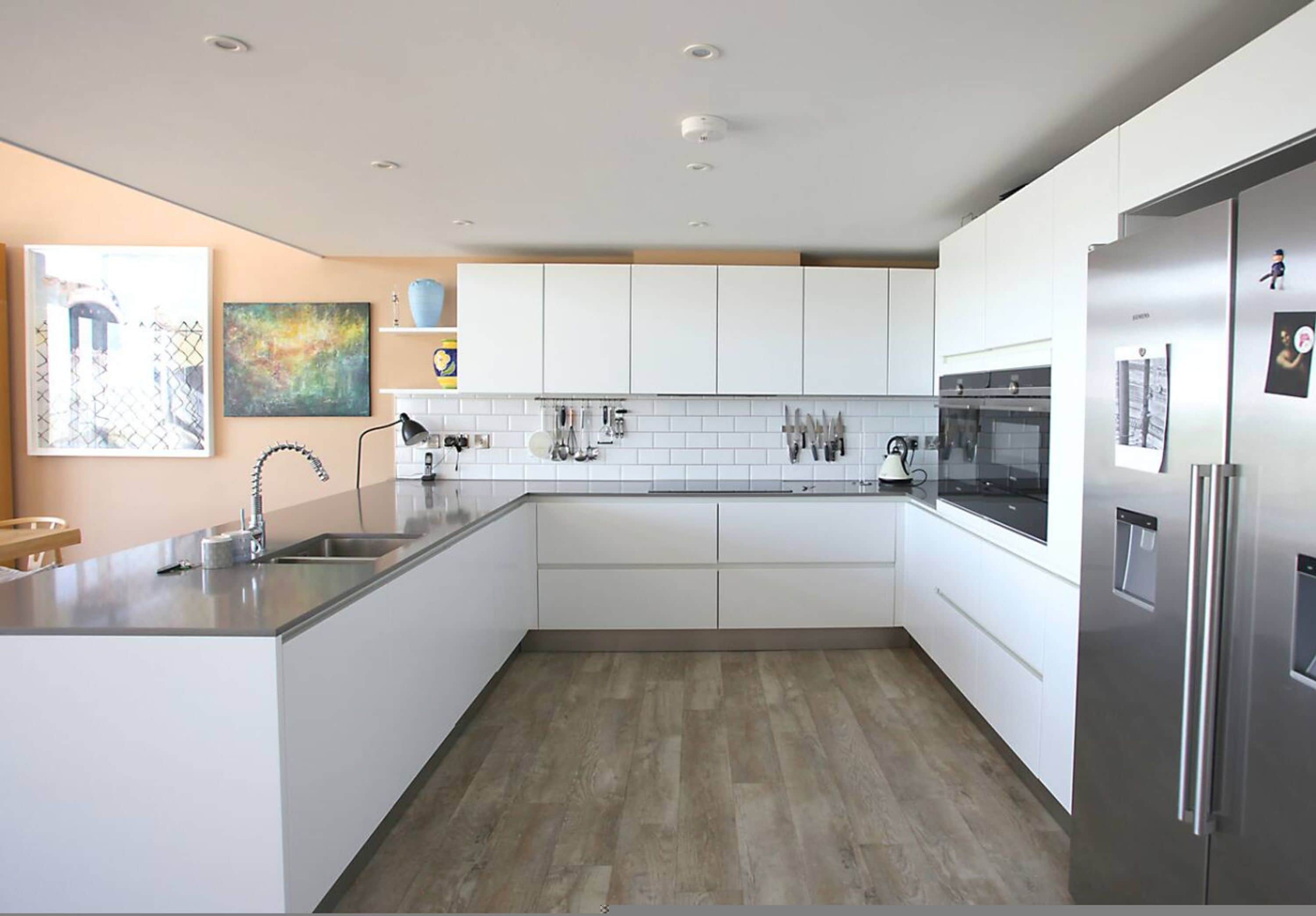 A modern kitchen with white cabinets, a stainless steel refrigerator, and a wooden floor.