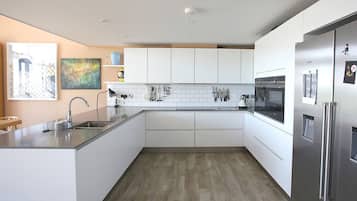 A modern kitchen with white cabinets, a stainless steel refrigerator, and a wooden floor.