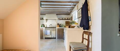 A narrow hallway leading to a kitchen with a wooden ceiling, a chair, and a wicker basket.