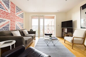 A modern living room with a sofa, armchair, TV, and a wall with text. - The Call of London 2 Bedroom Flat in Battersea (London)