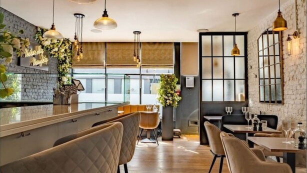 Zona de bar moderna con iluminación colgante, taburetes y vistas a la ciudad a través de amplios ventanales.