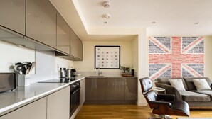 Una cocina moderna con armarios grises, un lavavajillas Bosch y un lavabo. Se observa un calendario enmarcado en la pared y una obra de arte con motivos de la Union Jack.