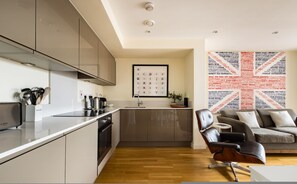 A modern kitchen with grey cabinets, a Bosch dishwasher, and a sink. There's a framed calendar on the wall and a Union Jack-themed artwork. - The Call of London 2 Bedroom Flat in Battersea (London)
