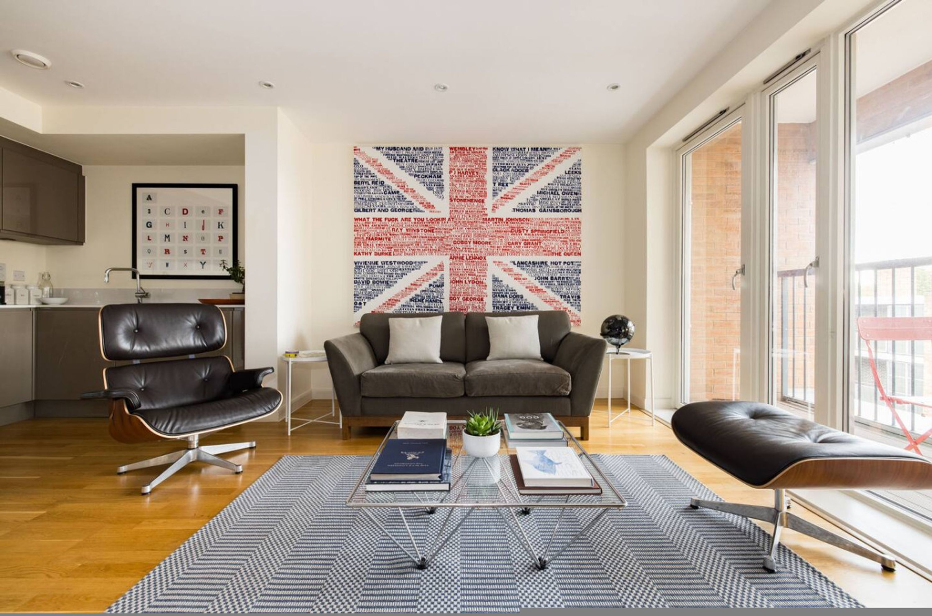 A modern living room with a sofa, a coffee table with books, a wall art piece, and a kitchen in the background.