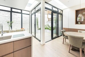 A modern kitchen with a large window, a dining area with a table and chairs, and a view of the outside. - Sunny in Chelsea Luxurious 3 Bedroom Chelsea Home (London)