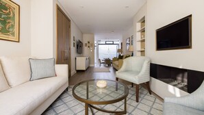 Una sala de estar moderna con sofá, sillón, mesa de centro de vidrio, chimenea y vistas al exterior.
