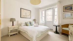 Une chambre bien rangée, avec un lit, des tables de chevet, une chaise et des œuvres d’art accrochées aux murs.