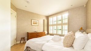 A bedroom with a bed, dresser, and a window with blinds. - A Gentle Riverside Charm 2 Bedroom Mews House (London)