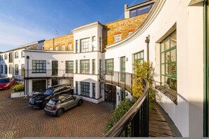 Un immeuble à plusieurs étages doté d’une façade incurvée, d’un toit en briques et d’une allée pavée où sont garées des voitures.