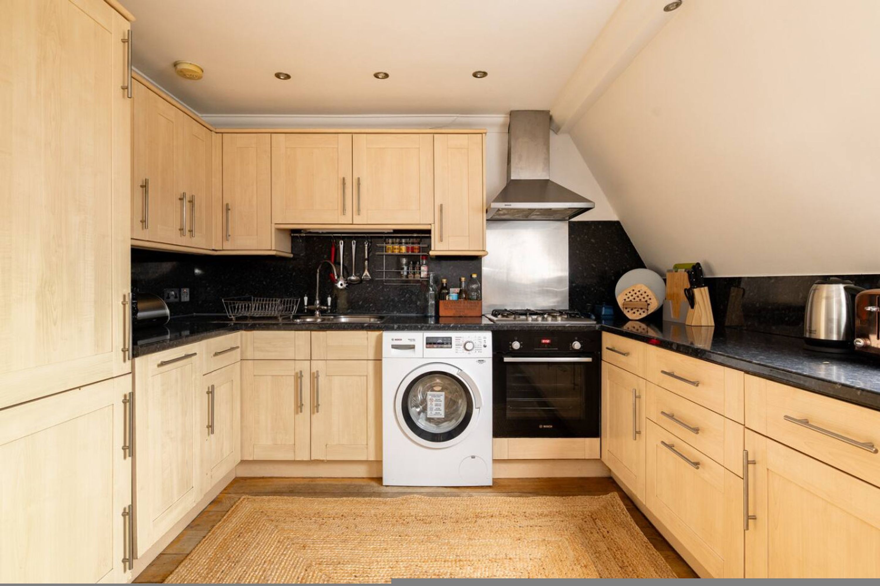 Une cuisine compacte avec des meubles en bois, un lave-linge, une cuisinière et un évier.