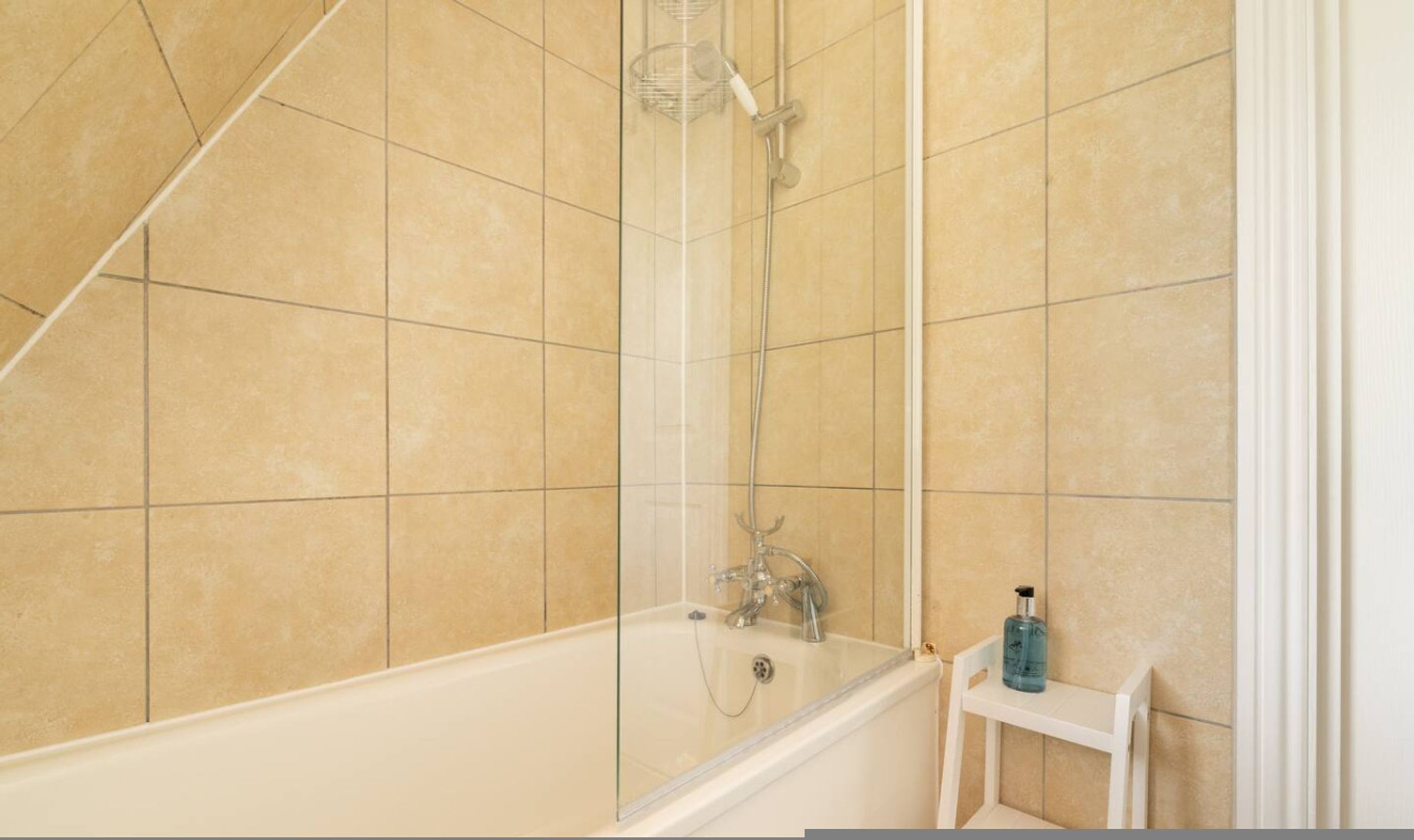 A bathroom with a bathtub, shower, and a small shelf with a bottle.